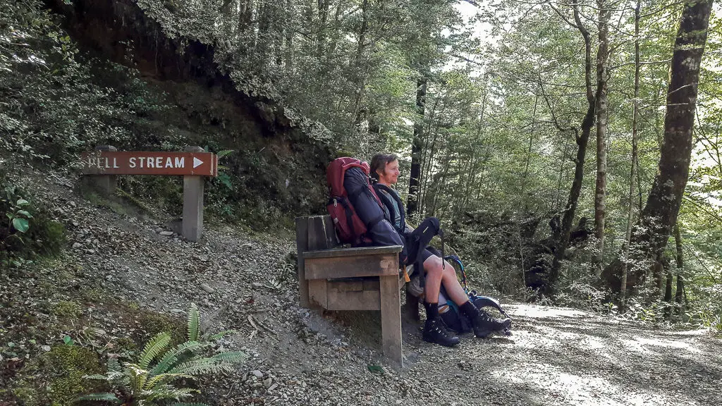 Man sitting on a wooden bench in the forest with a sign pointing towards Pell Stream