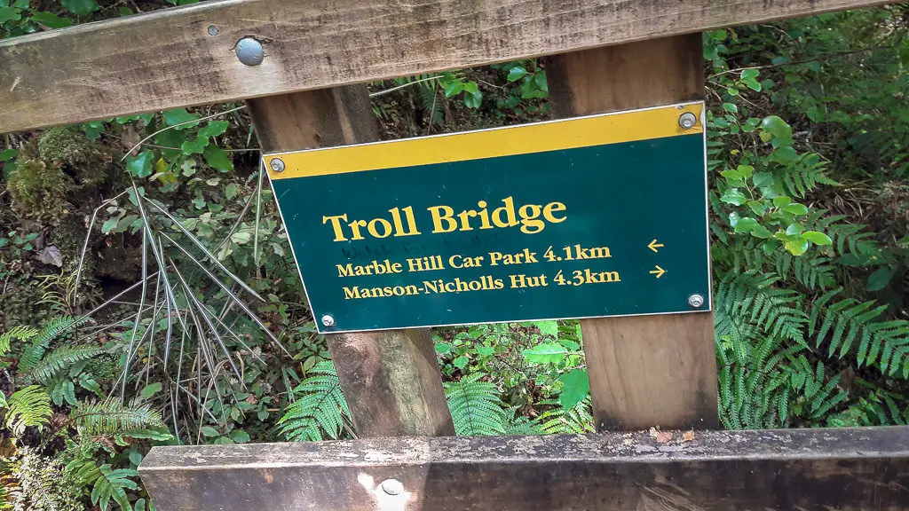 DOC sign on a wooden bridge with "Troll Bridge" written on the sign along with timing for Marble Hill carpark and Manson-Nicholls Hut