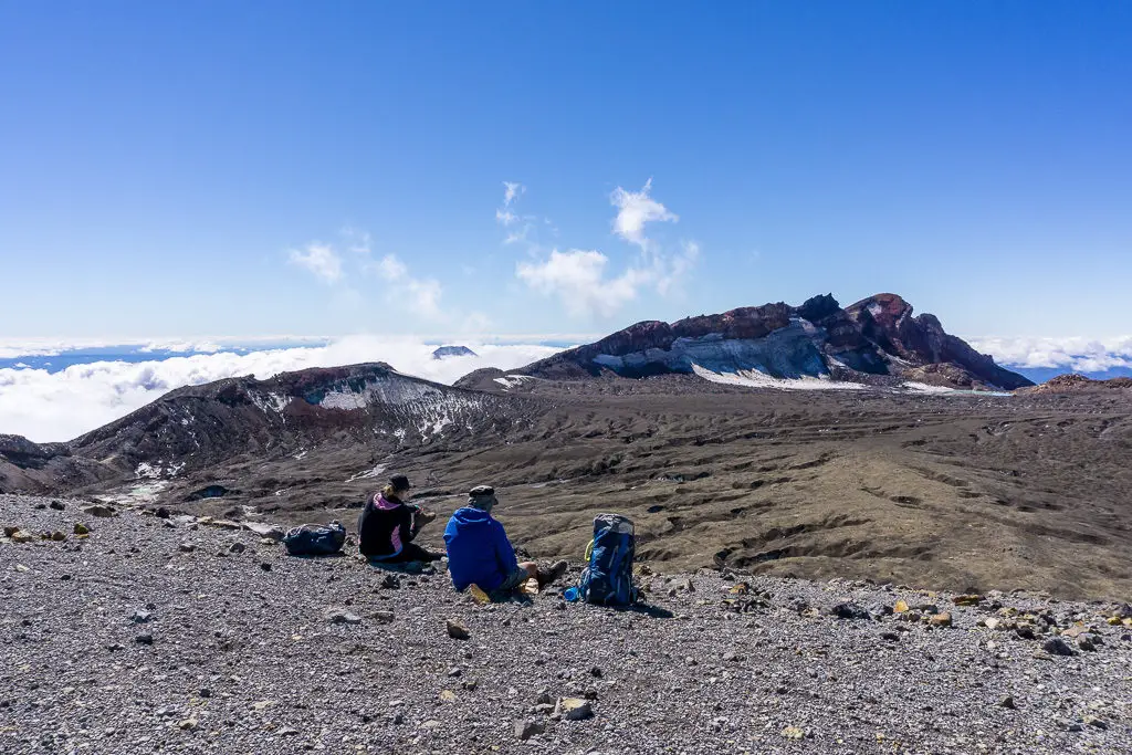 Trampers sitting on volcanic rocks having lunch next to Mt Ruapehu Crater Lake