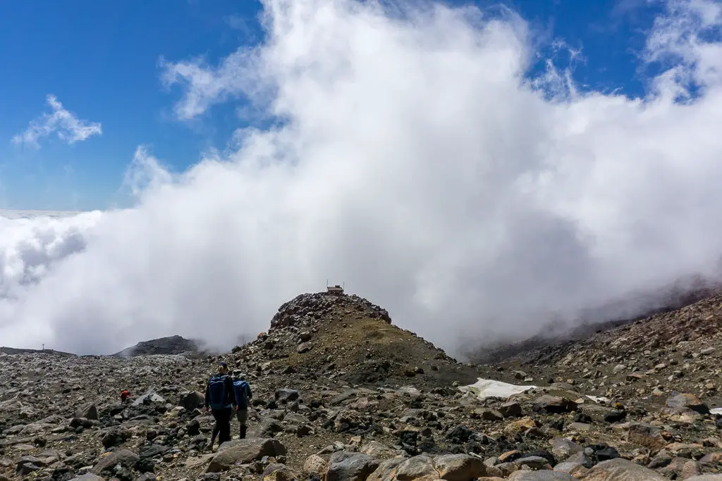 Trampers climbing down Mt Ruapehu with cloud building below