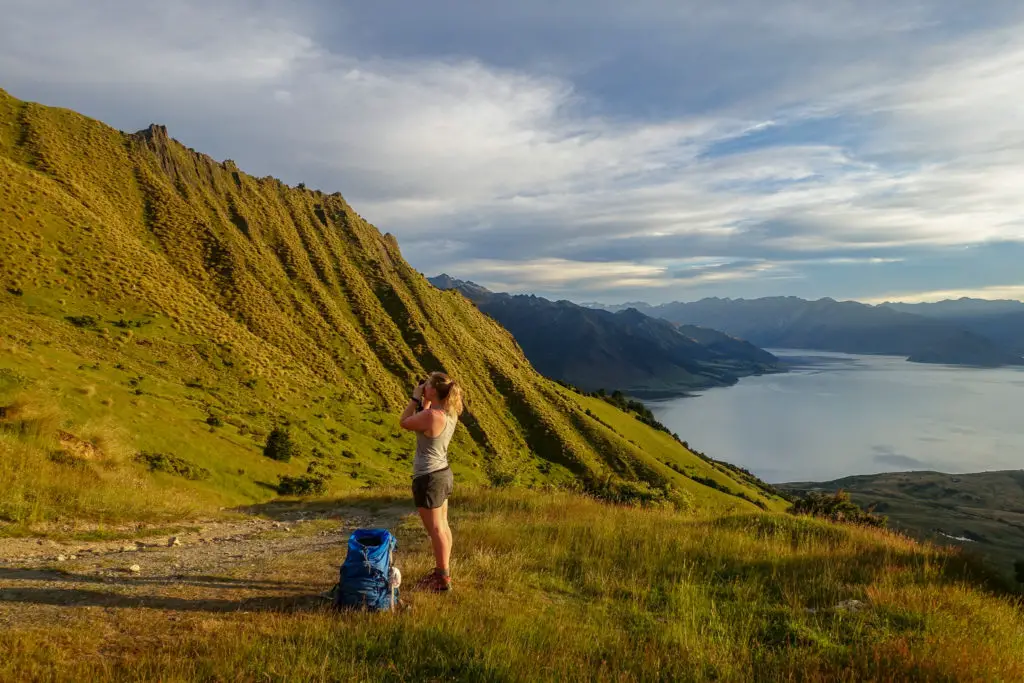 Woman taking photos of Isthmus Peak at dawn with Lake Hawea in the background