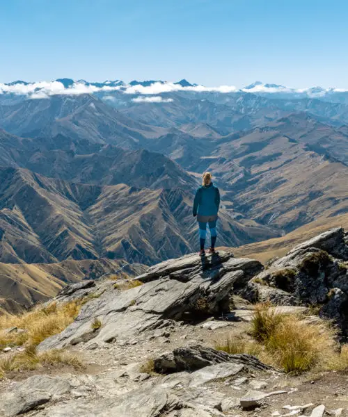Female hiker standing on the summit of Ben Lomond looking towards the Southern Alps and Mt Aspiring
