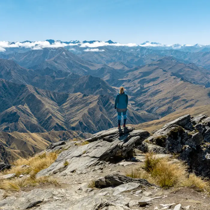 Female hiker standing on the summit of Ben Lomond looking towards the Southern Alps and Mt Aspiring