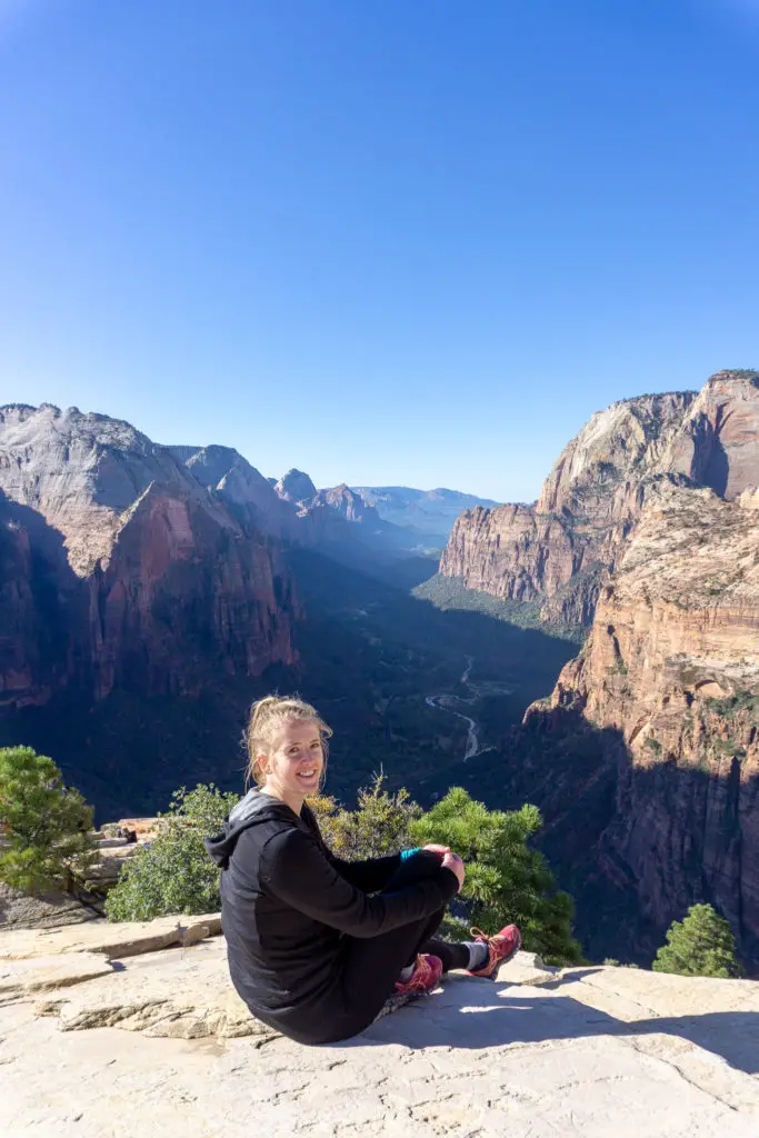 Female hiker sitting on top of Angel's Landing in Zion National Park with a giant smile on her face