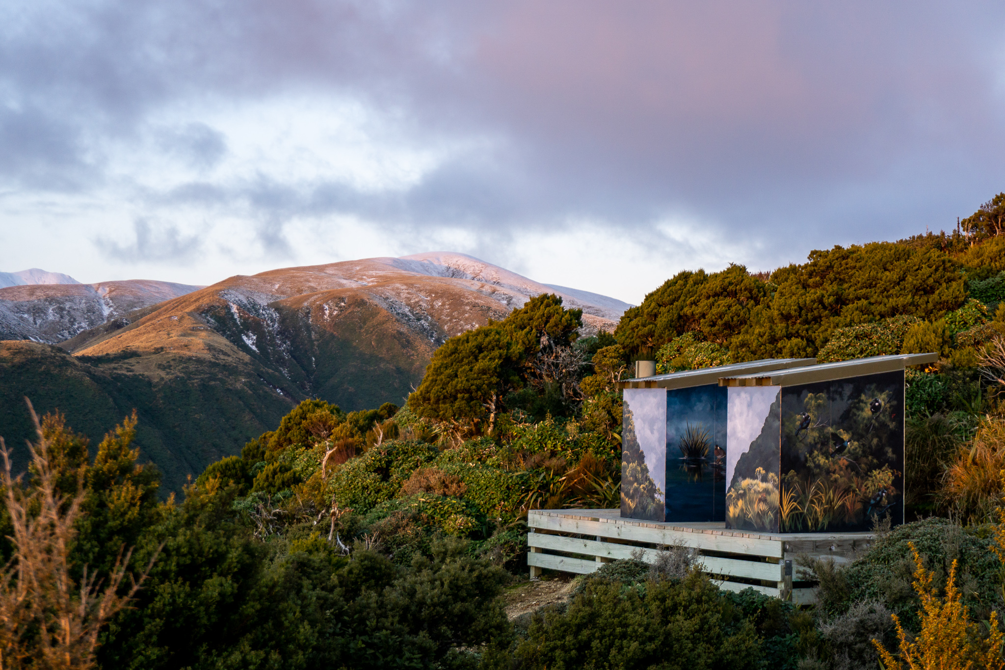 Shot of the beautifully painted Rangiwahia Hut long-drop toilets at sunset with snow on the hills behind