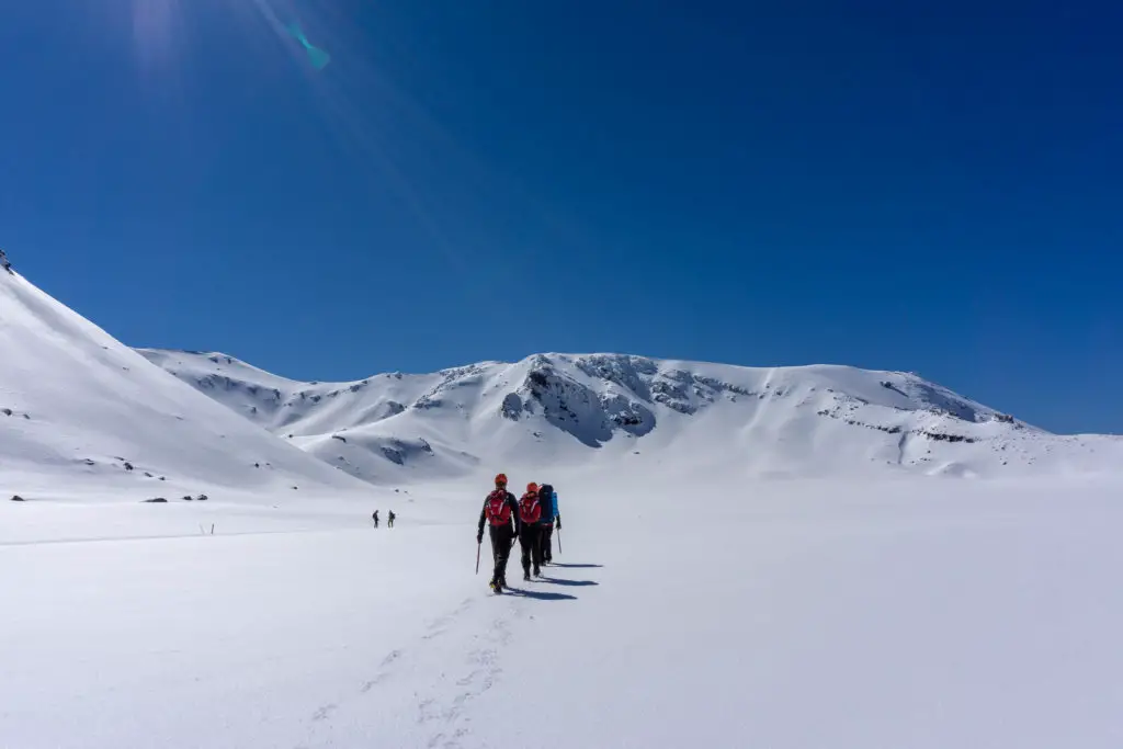 Hikers carrying ice axes walking along South Crater towards Red Ridge on the Tongariro Crossing in winter surrounded by snow