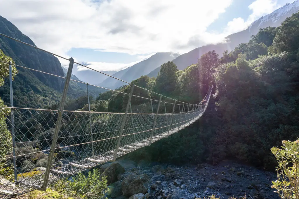 High and long swing bridge over Shiels Creek on the Copland Track with sun setting along the blue-haze ridge -ines in the background