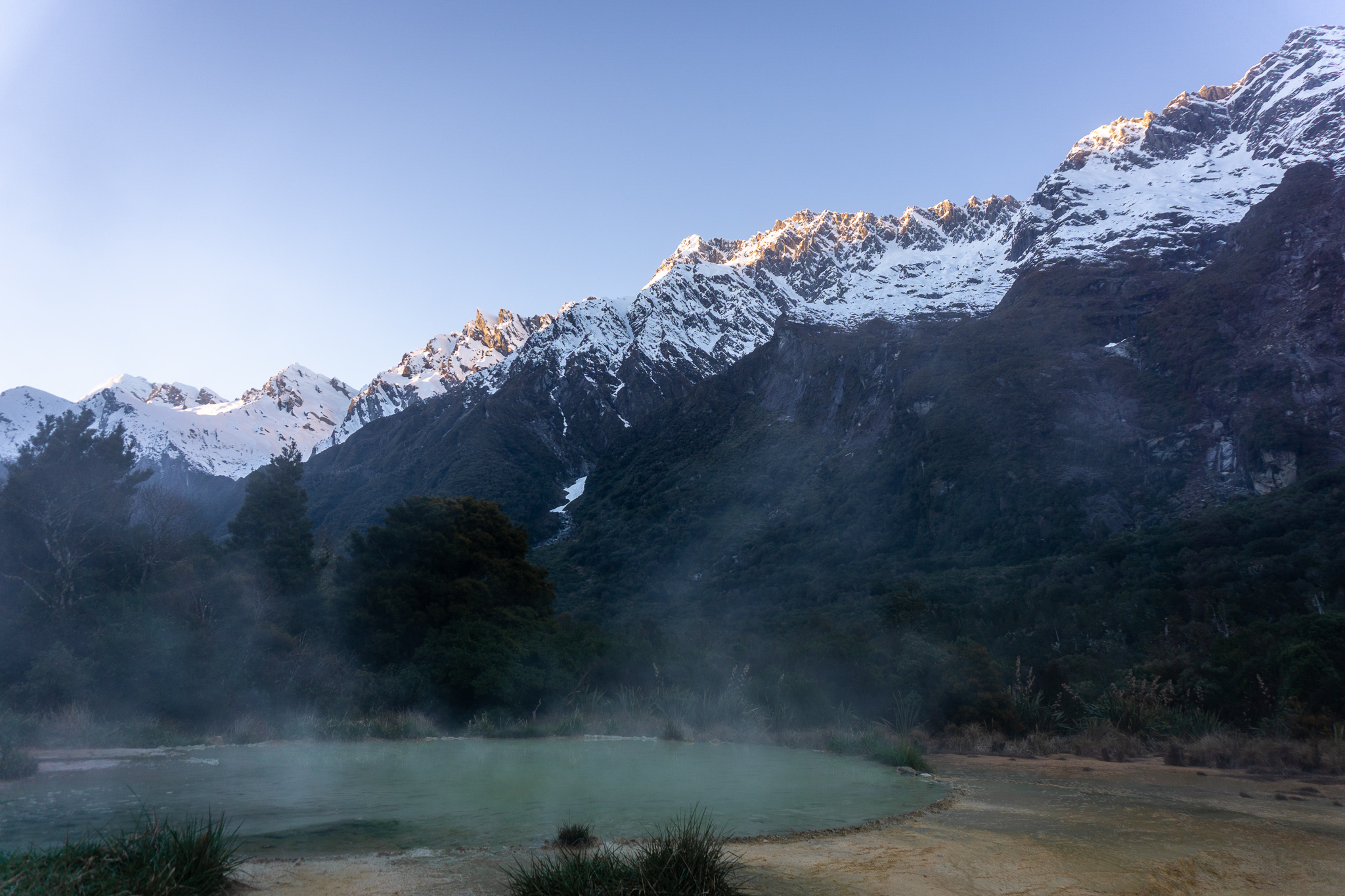 Welcome Flat natural hotpools steaming with dawn light just hitting the tops of the snowcapped mountains in the background