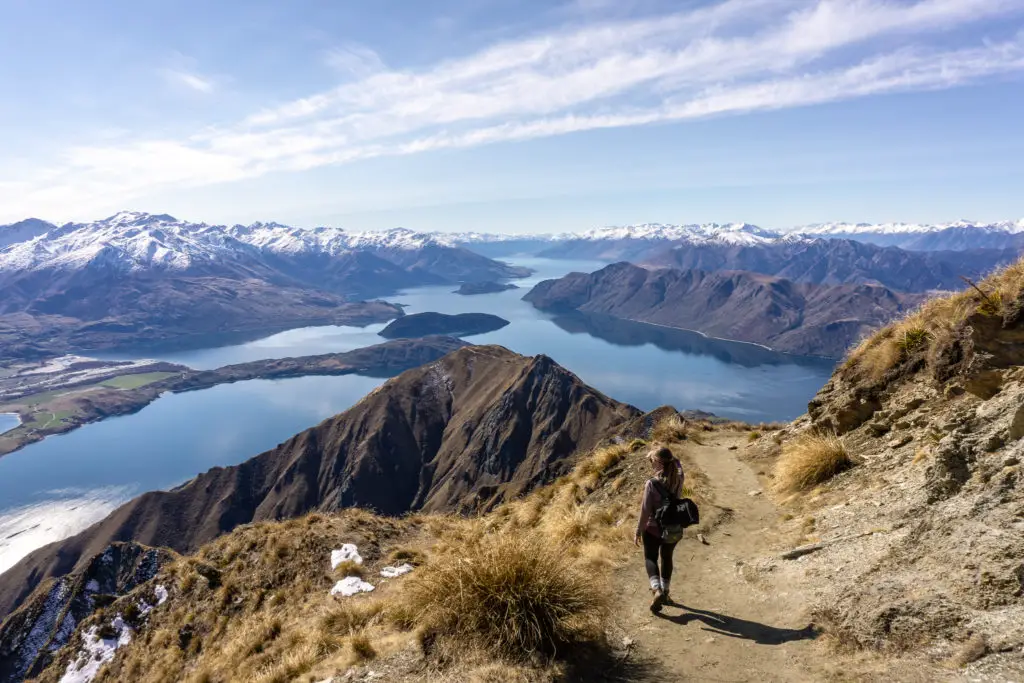 Female hiker walking down from the summit of Roy's Peak track with Lake Wanaka, and mountains in the background
