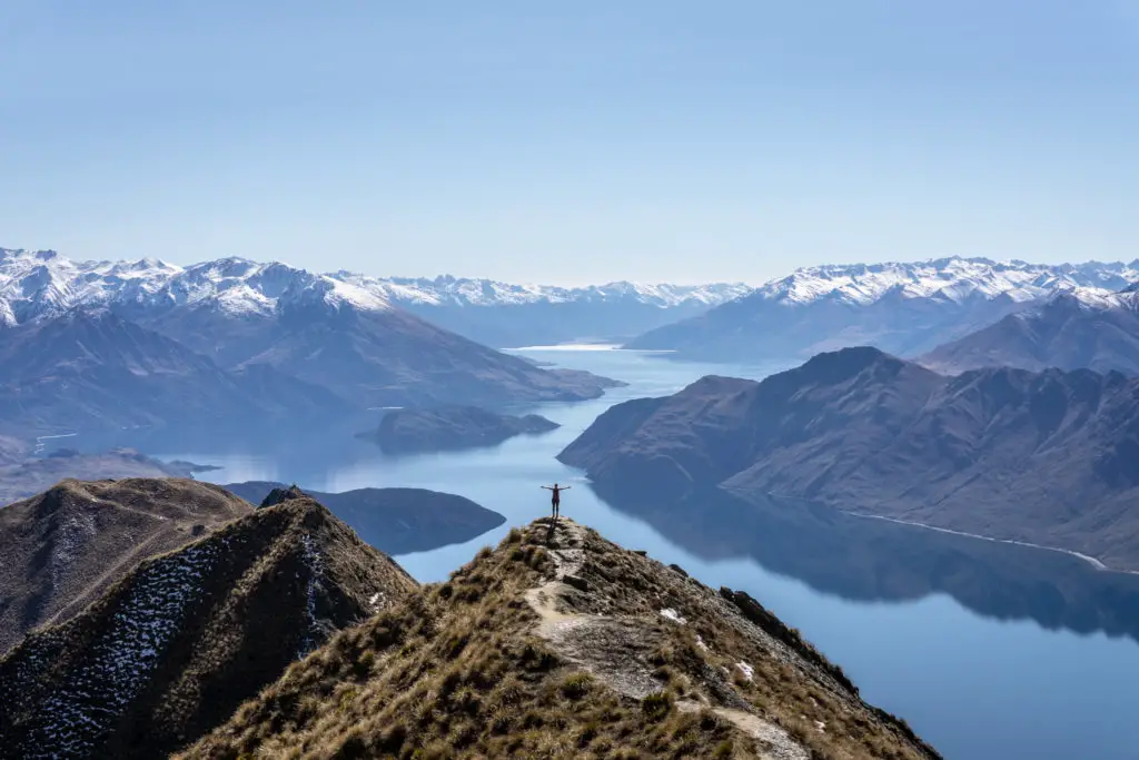 "That shot" of Roys Peak viewpoint with a person standing silhouetted against the reflective lake with arms held up