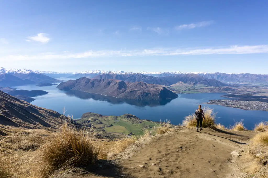 Female hiker walking down Roys Peak track with Lake Wanaka and mountains in the background
