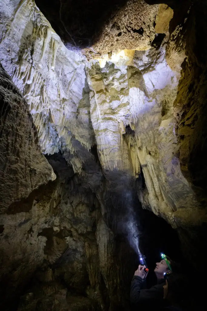 Cavers shining flashlights up onto the cave roof, with interesting rock formations including stalactites hanging rom the roof