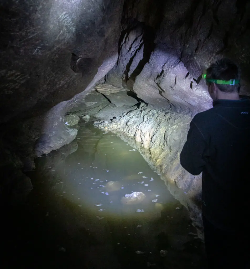 Caver shining a torchlight onto a flooded underground passage