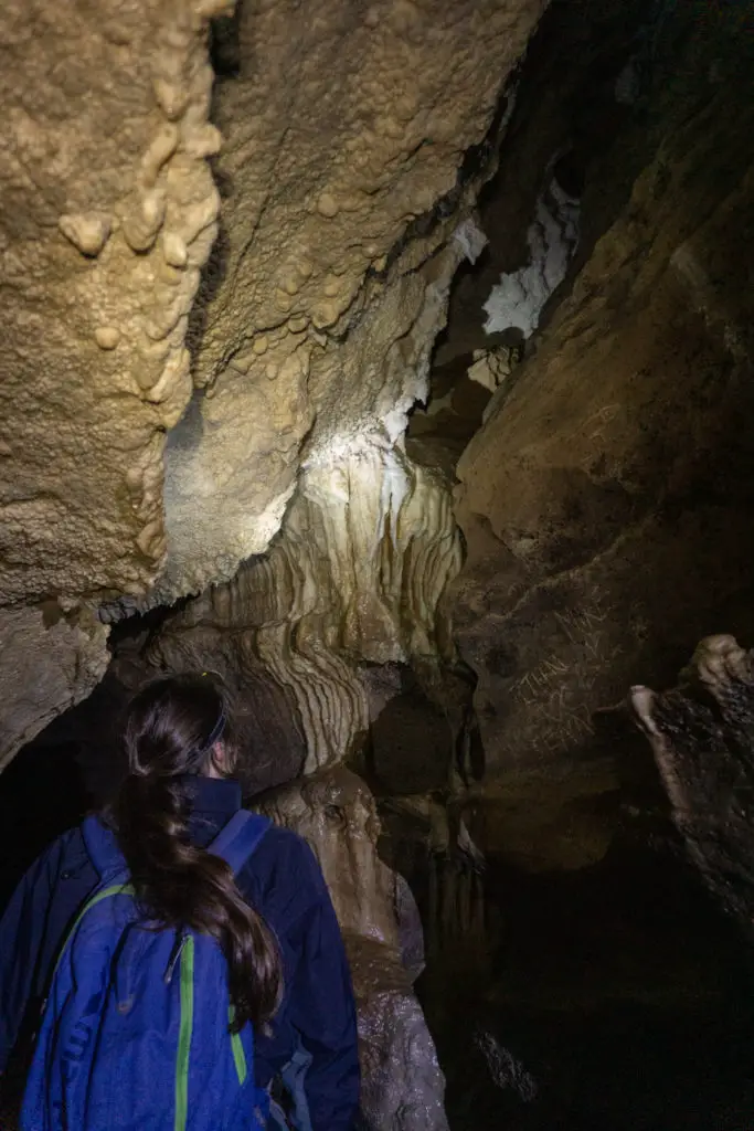 Female caver looking up at the roof of the cave and illuminating stalactites and flowstone