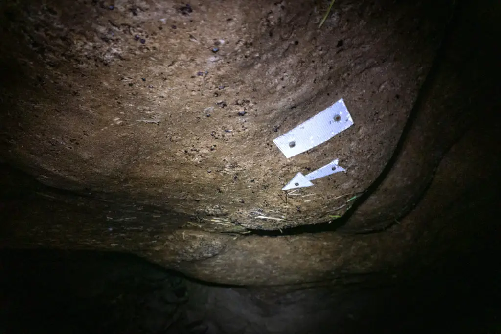 Flashlight illuminating white marker and arrow pointing to the left, stuck to the roof of the cave