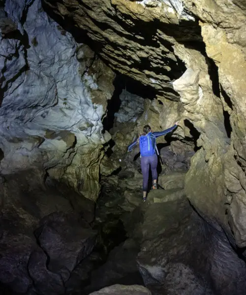 Flashlight shining on a caver negotiating a tunnel in Clifden Caves