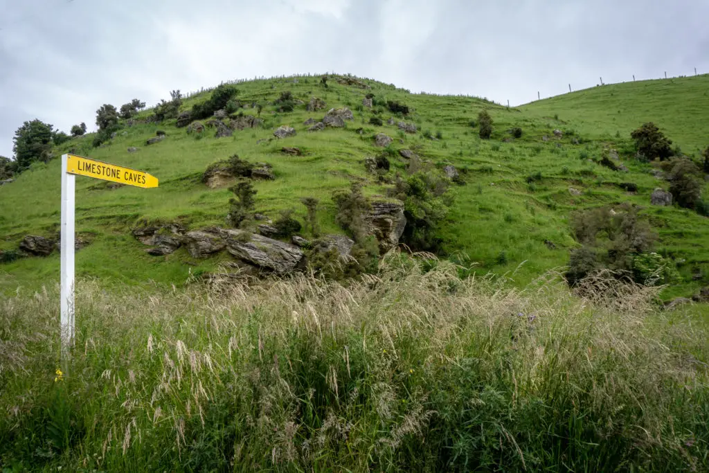 Yellow road sign pointing to the Clifden Caves in a farmer's paddock