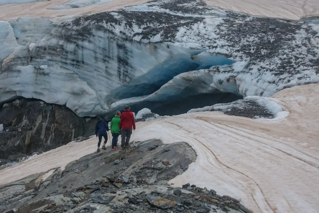 Three trampers standing on the edge of Brewster Glacier looking at an ice cave