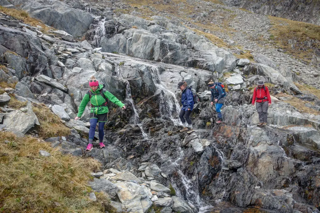 Four trampers crossing a steep section of rock and little waterfalls between Brewster Hut and Brewster Glacier