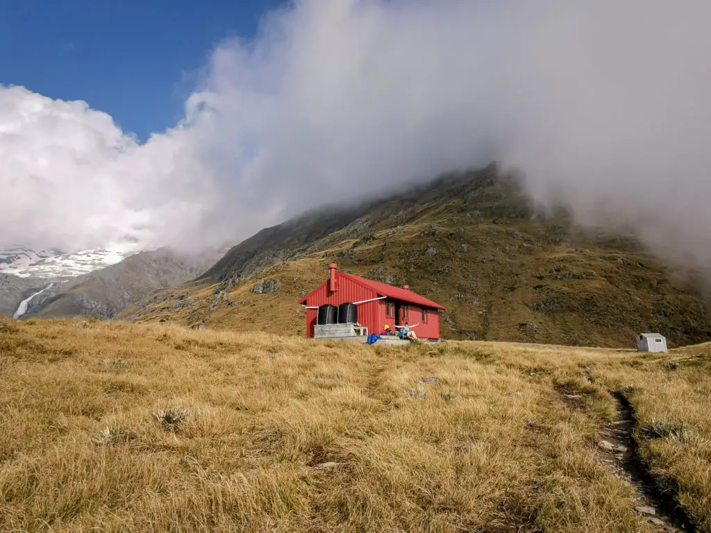 Brewster Hut as seen from the track, with a waiting tramper celebrating arriving