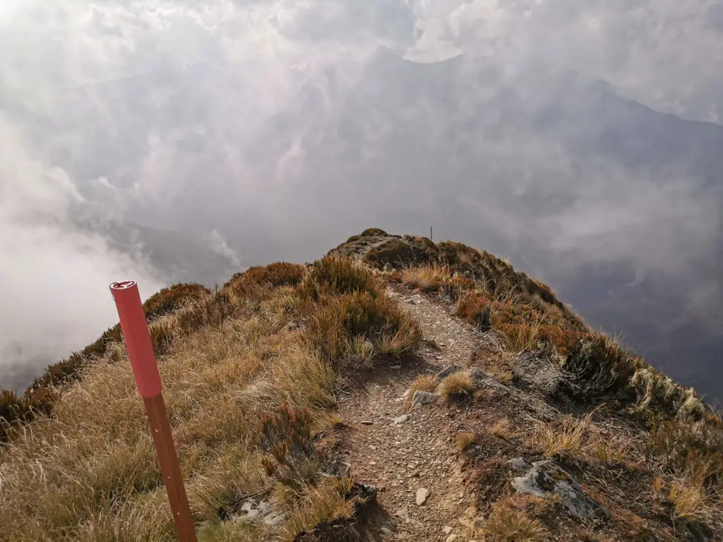 View of the tramping track with pole markers leading down the ridge with smoky clouds hovering in the air
