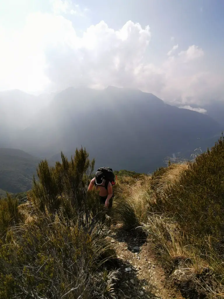 Female tramper climbing up a track with hazy mountains in the background
