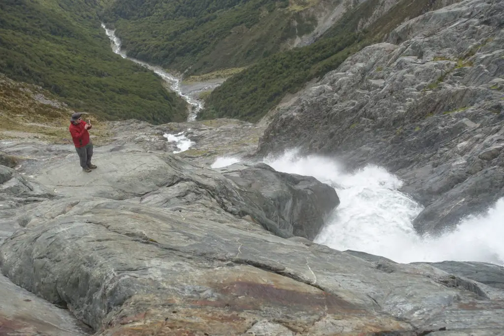 Male tramper standing next to waterfall cascading down to Pyke Creek