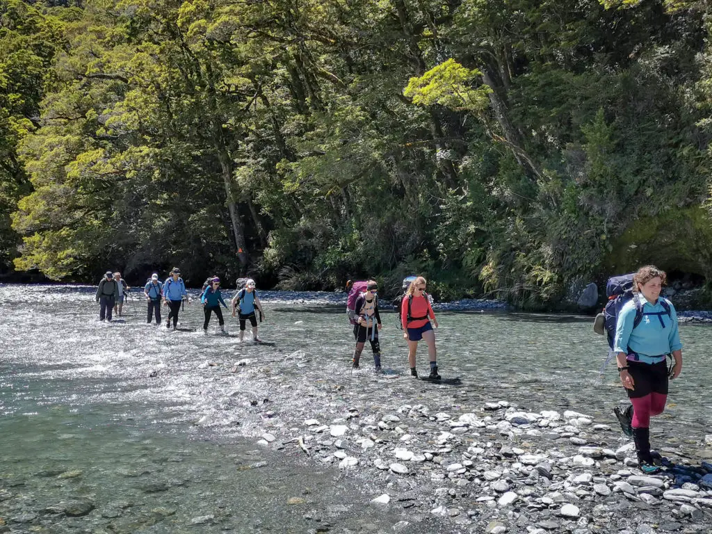 Group of trampers crossing the Haast River at low flow, with triangle marker for Brewster track in the background