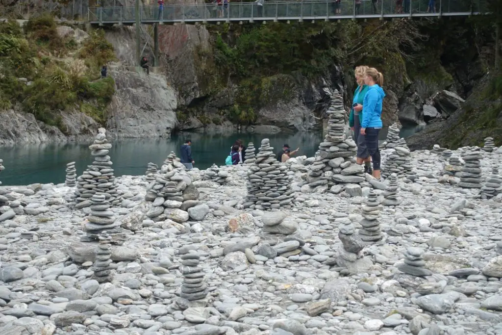 Stacks of rocks (cairns) littering the stony beach by the Blue Pools, two women and a bridge in the background
