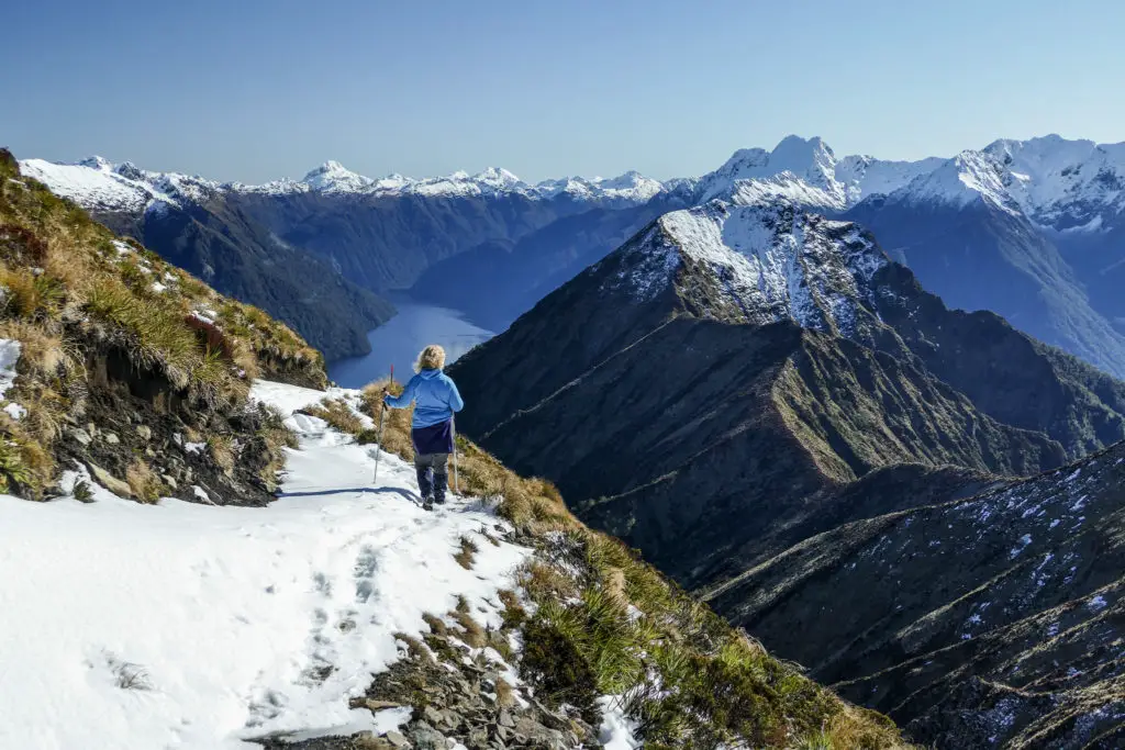 Female hiker in snow walking the Kepler Track with views towards Lake Te Anau and the surrounding mountains