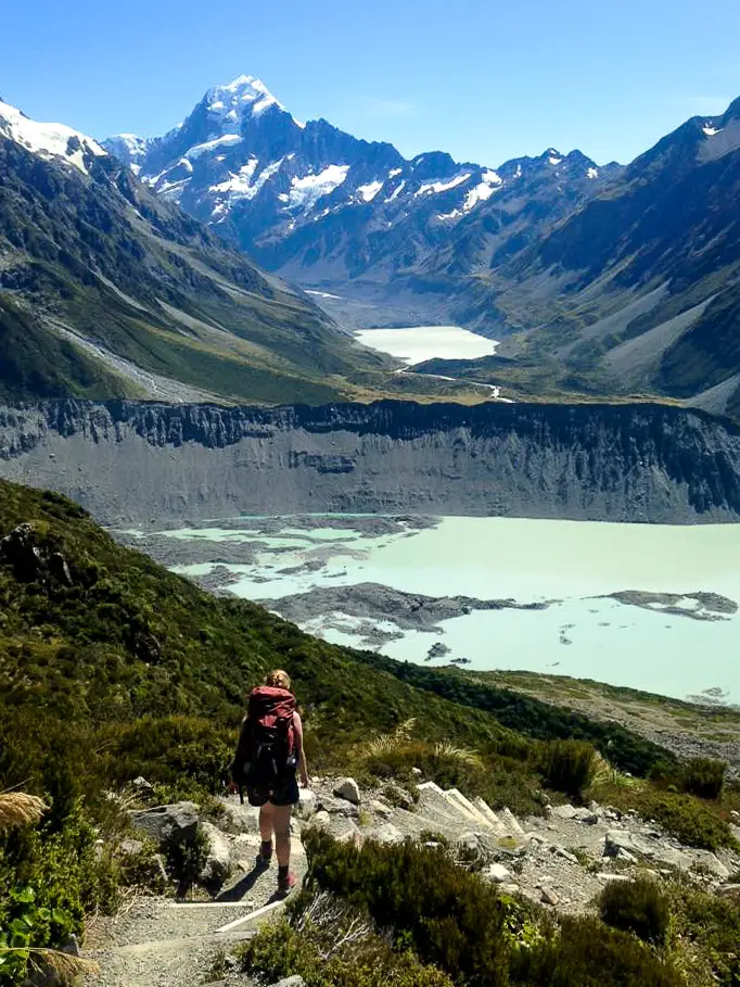 Female hiker walking down stairs with a glacial lake in the background and Aoraki / Mt Cook in the distance