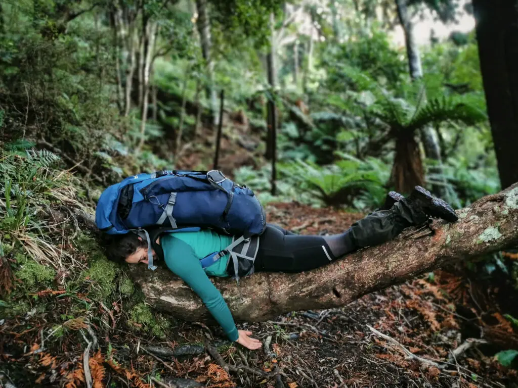 Woman lying face-down on log with pack on her back on the track between Freshwater Hut and North Arm Hut on Stewart Island