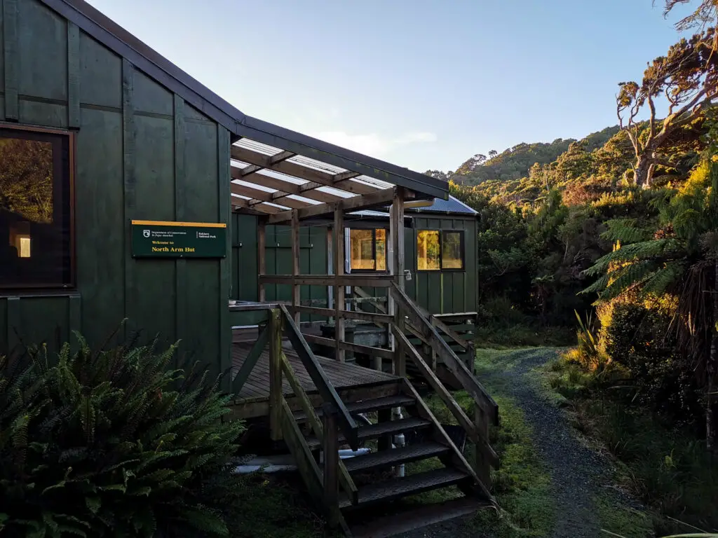 North Arm Hut on Stewart Island with sunset rays highlighting the bush around it in winter