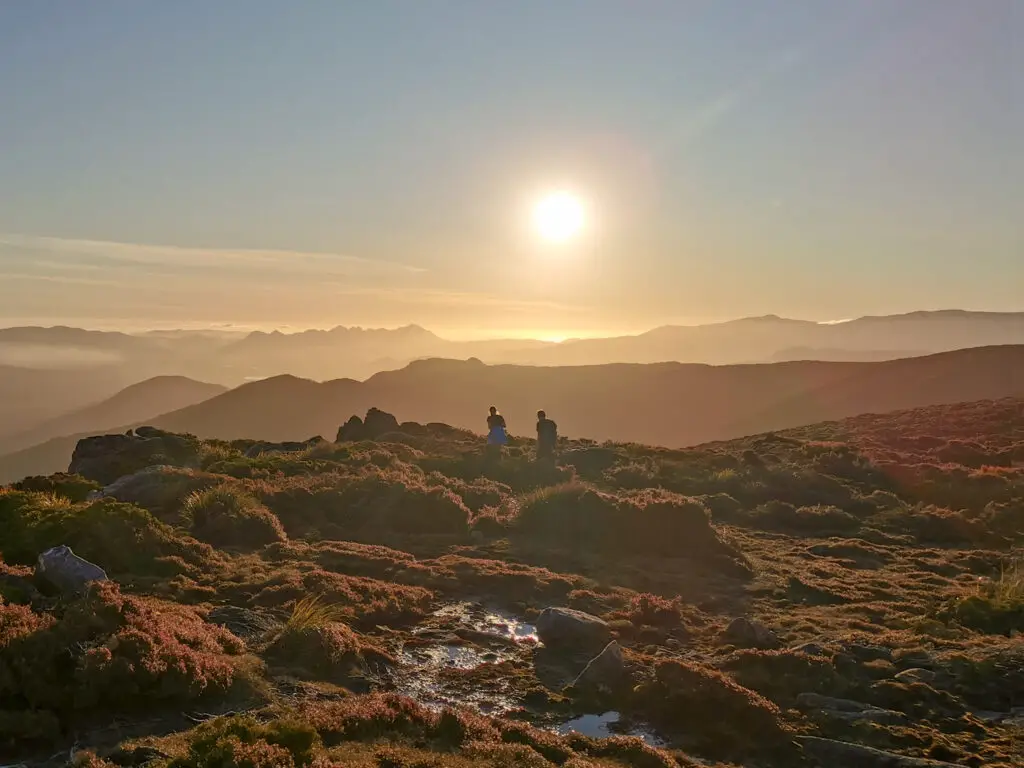 Two hikers walking into the sunset with ridge lines fading into the background