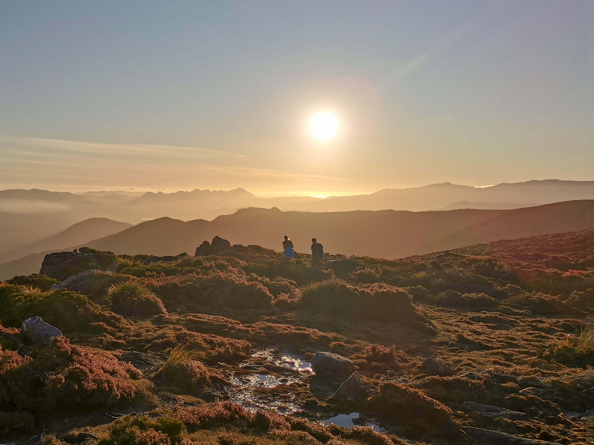 Two hikers walking into the sunset with ridge lines fading into the background