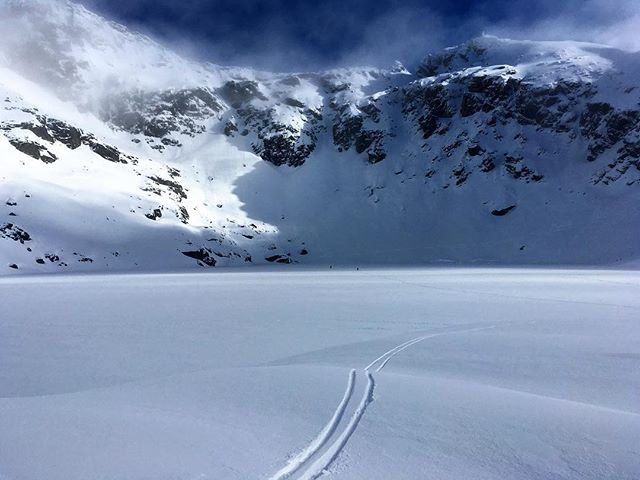 Ski tracks in virgin snow across Lake Alta with cloudy Double Cone in the background
