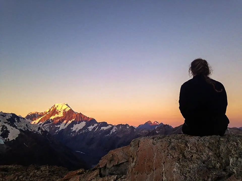 Lady sitting on a rock next to Mueller Hut watching the sun set on Aoraki / Mt Cook