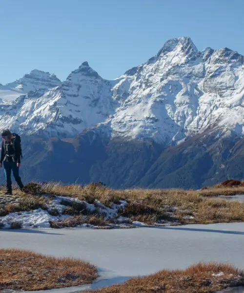 Female hiker walking next to a frozen tarn above Sugarloaf Pass with Mt Earnslaw in the background - perfect winter tramping trip