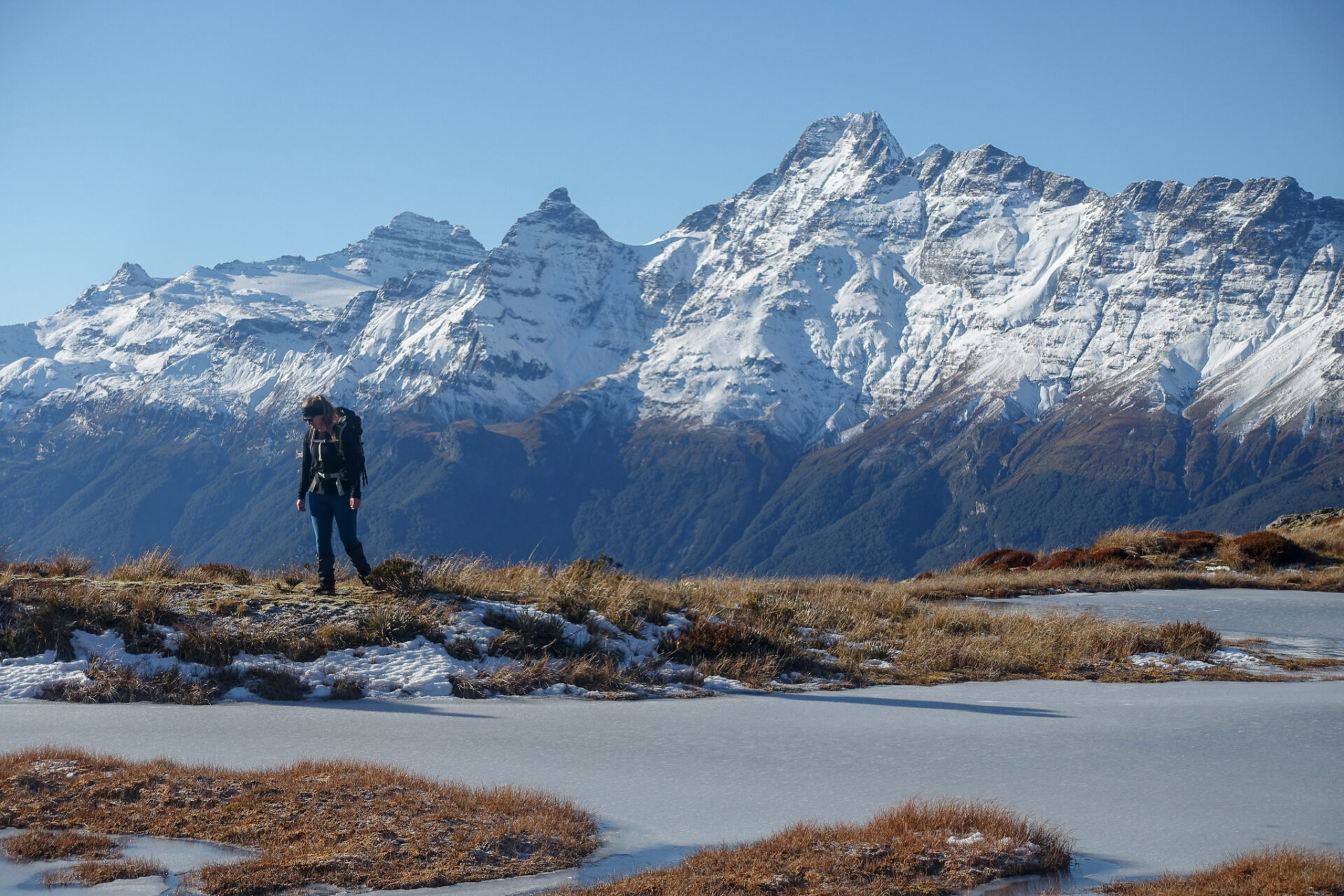 Female hiker walking next to a frozen tarn above Sugarloaf Pass with Mt Earnslaw in the background - perfect winter tramping trip