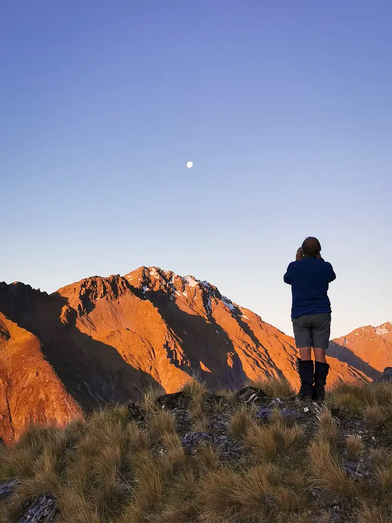 Man taking a photo of the full moon in the mountains at sunset