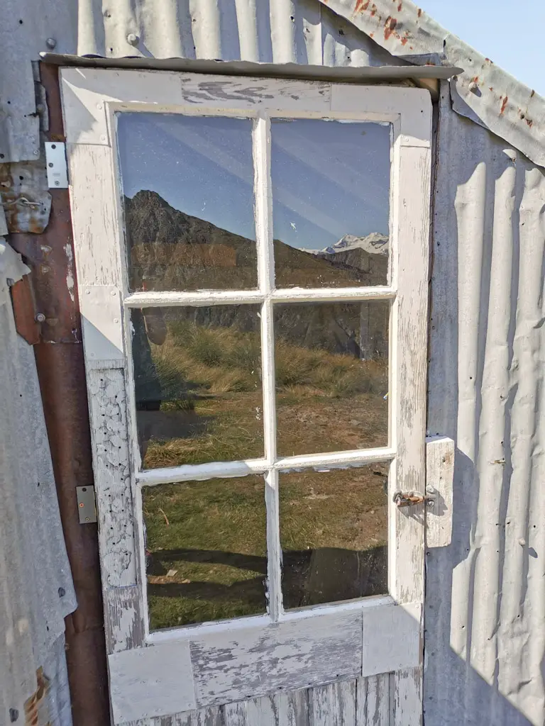 Door of Heather Jock Hut with mountains reflecting in the glass