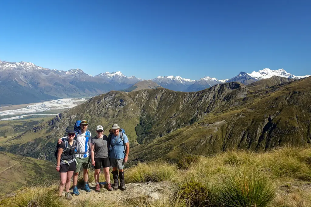 Four hikers standing outside Heather Jock Hut with views to Glenorchy in the background