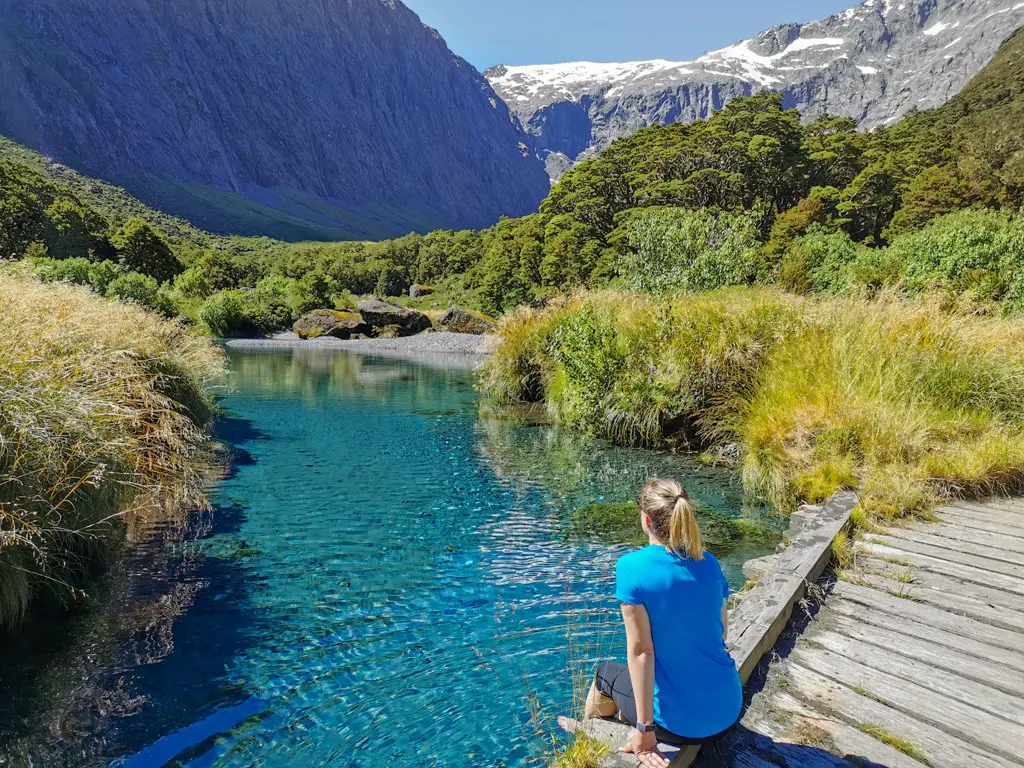 Lady sitting on a bridge over beautiful blue water at the start of the Gertrude Valley
