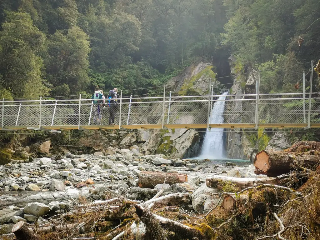 Giant Gate Falls on the Milford Great Walk with hikers standing on the swingbridge in the foreground