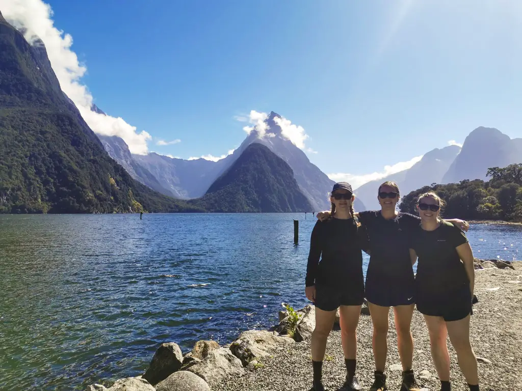 Three ladies standing on the pier at Milford Sound on a sunny day with Mitre Peak in the background