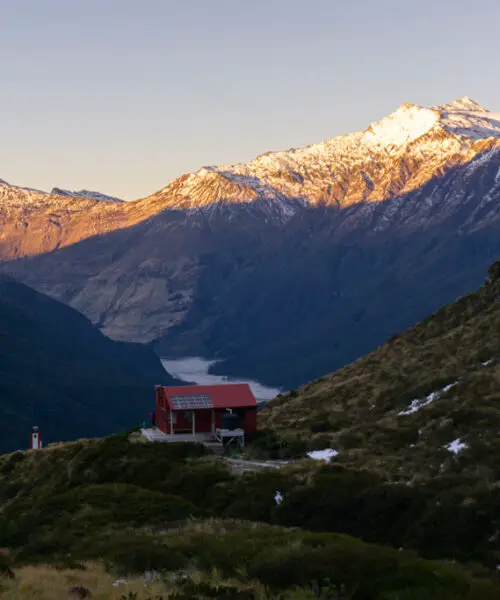 Liverpool Hut as the sun rises, with the Matukituki Valley and Aspiring Hut in the background