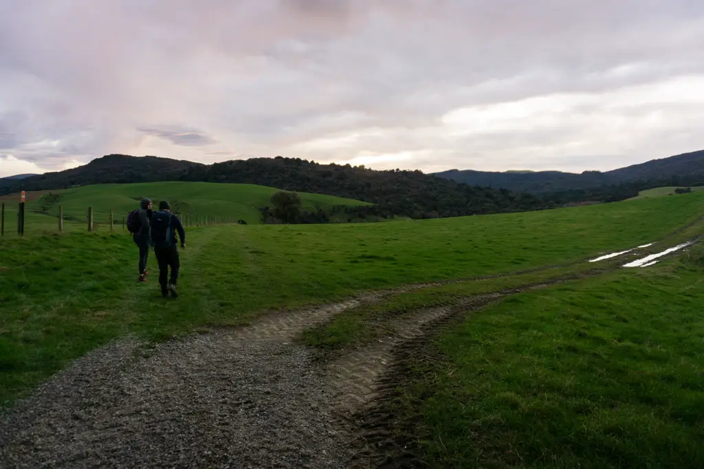 Two people walking across paddocks in the Hokonui Hills