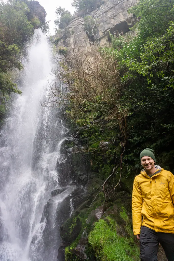 Man in yellow rain jacket standing in front of Makarewa Falls in the Hokonui Hills