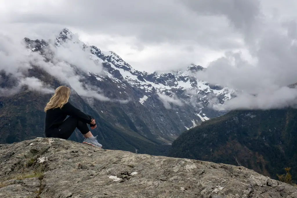 Woman sitting on a rock on top of Key Summit in Fiordland National Park looking across to Lake Marian