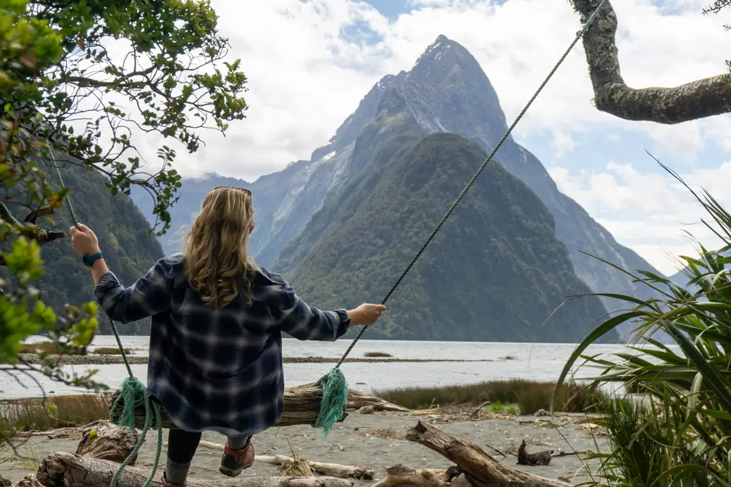 Woman swinging on a rope swing at Milford Sound in front of Mitre Peak